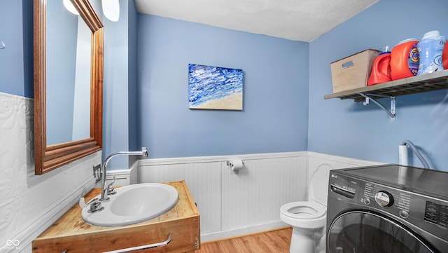 bathroom with toilet, sink, a textured ceiling, hardwood / wood-style flooring, and washer / clothes dryer