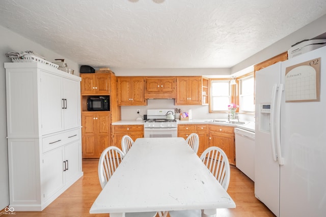 kitchen featuring sink, a textured ceiling, white appliances, and light wood-type flooring