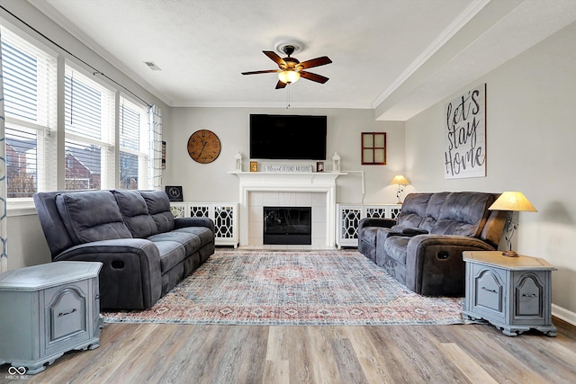 living room featuring crown molding, light hardwood / wood-style floors, a tile fireplace, and ceiling fan