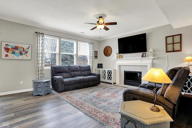 living room with crown molding, ceiling fan, hardwood / wood-style floors, a textured ceiling, and a tiled fireplace