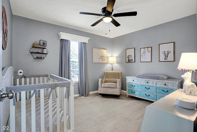 carpeted bedroom with a crib and ceiling fan