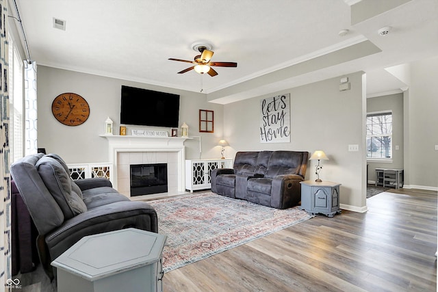 living room with a tiled fireplace, crown molding, hardwood / wood-style floors, and ceiling fan