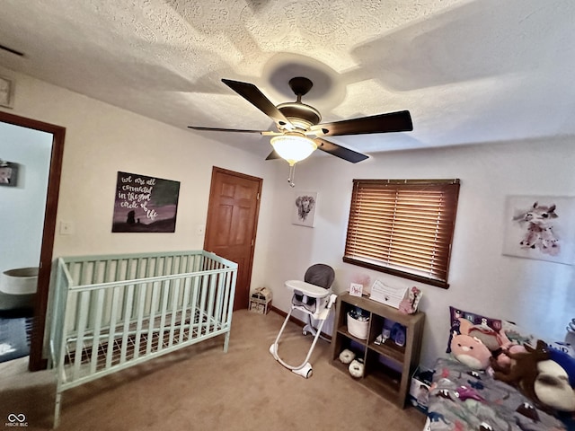 carpeted bedroom with ceiling fan, a nursery area, and a textured ceiling