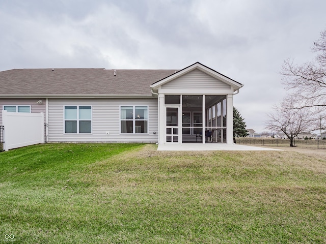 rear view of property featuring a sunroom, a shingled roof, fence, and a lawn