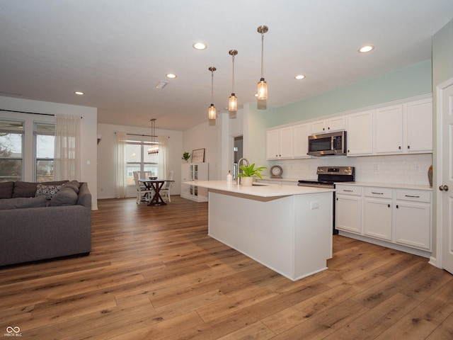 kitchen with stainless steel appliances, open floor plan, light wood-style floors, and decorative backsplash