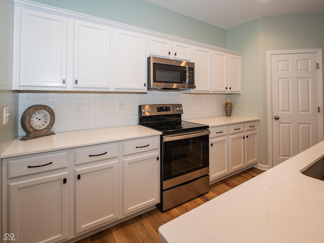 kitchen with light countertops, backsplash, light wood-style flooring, appliances with stainless steel finishes, and white cabinets