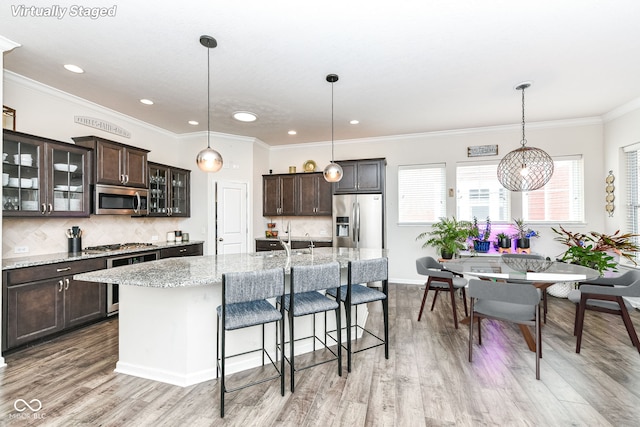 kitchen featuring dark brown cabinetry, light stone counters, decorative light fixtures, appliances with stainless steel finishes, and a kitchen island with sink