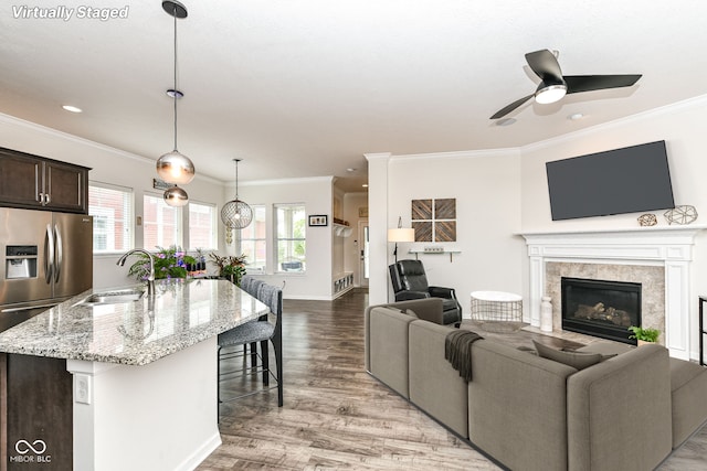 living room with sink, a premium fireplace, ceiling fan, ornamental molding, and light wood-type flooring