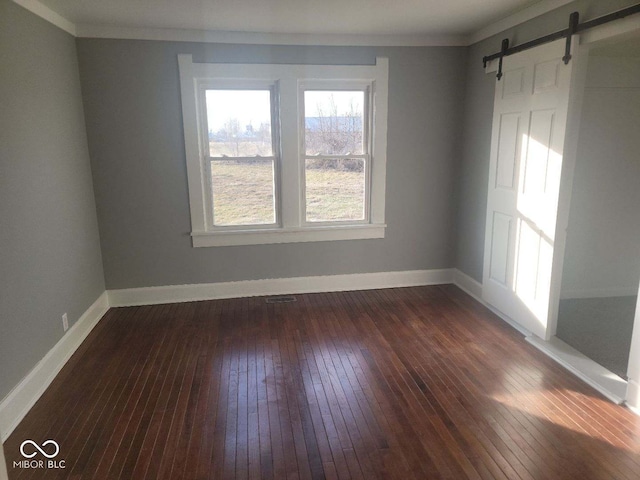 empty room with crown molding, dark wood-type flooring, and a barn door