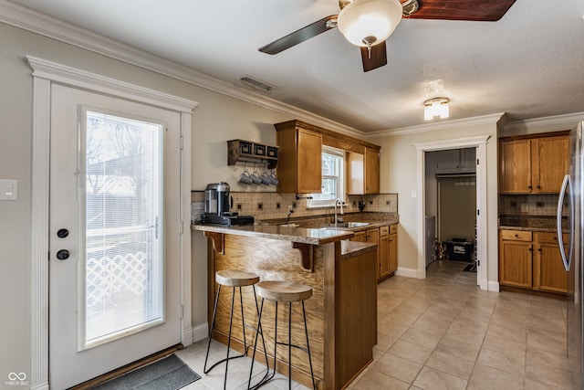 kitchen with sink, a breakfast bar area, crown molding, kitchen peninsula, and dark stone counters