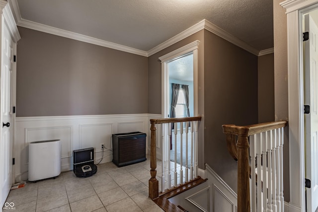 hall with light tile patterned flooring, ornamental molding, and a textured ceiling