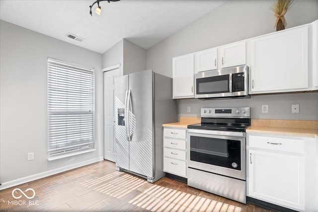 kitchen with lofted ceiling, light hardwood / wood-style flooring, appliances with stainless steel finishes, a textured ceiling, and white cabinets