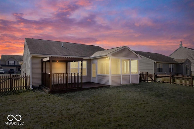 back house at dusk featuring a wooden deck and a lawn