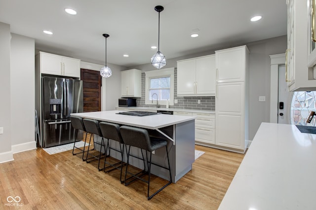 kitchen with pendant lighting, stainless steel fridge, a breakfast bar, white cabinets, and a kitchen island