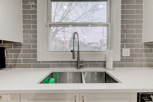 interior details with white cabinetry, sink, and backsplash