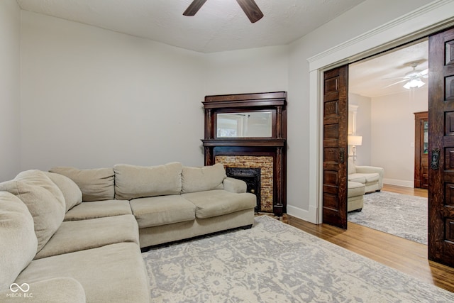 living room with hardwood / wood-style floors, a stone fireplace, a textured ceiling, and ceiling fan