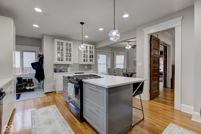 kitchen with a breakfast bar area, gas range, white cabinetry, a center island, and hanging light fixtures