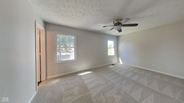 empty room featuring ceiling fan, light colored carpet, and a textured ceiling