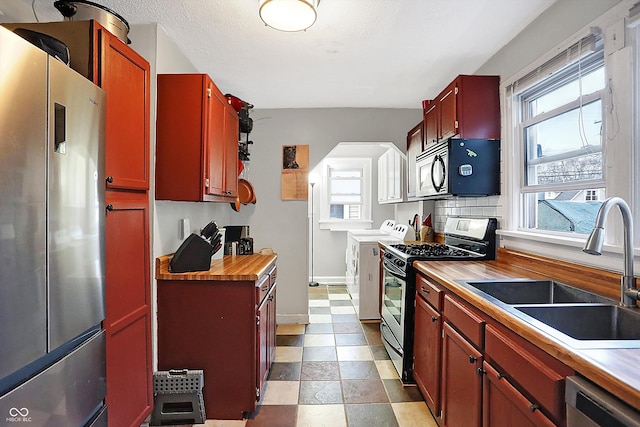 kitchen featuring wood counters, sink, appliances with stainless steel finishes, a wealth of natural light, and washer and clothes dryer