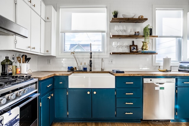 kitchen with butcher block countertops, appliances with stainless steel finishes, a wealth of natural light, white cabinets, and blue cabinets