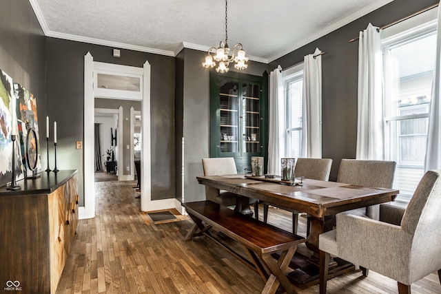 dining space with hardwood / wood-style floors, a textured ceiling, ornamental molding, and a chandelier