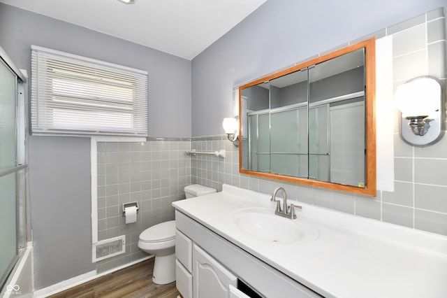 full bathroom with tile walls, shower / bath combination with glass door, hardwood / wood-style flooring, vanity, and toilet