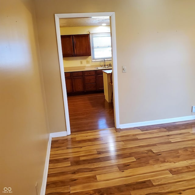 corridor featuring baseboards, a sink, and light wood finished floors