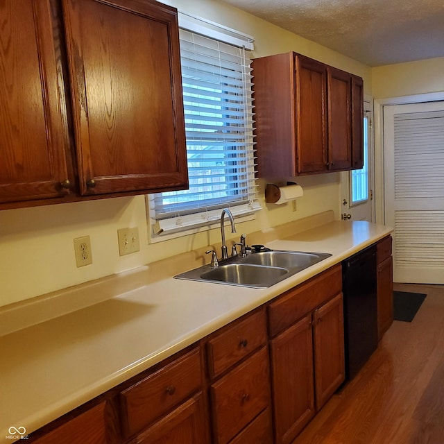 kitchen with light countertops, a sink, a textured ceiling, wood finished floors, and dishwasher