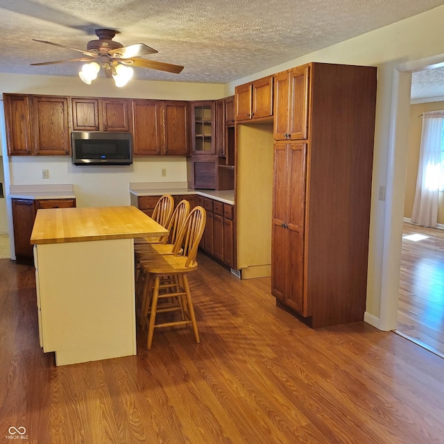 kitchen with dark wood-style floors, stainless steel microwave, a textured ceiling, and brown cabinetry