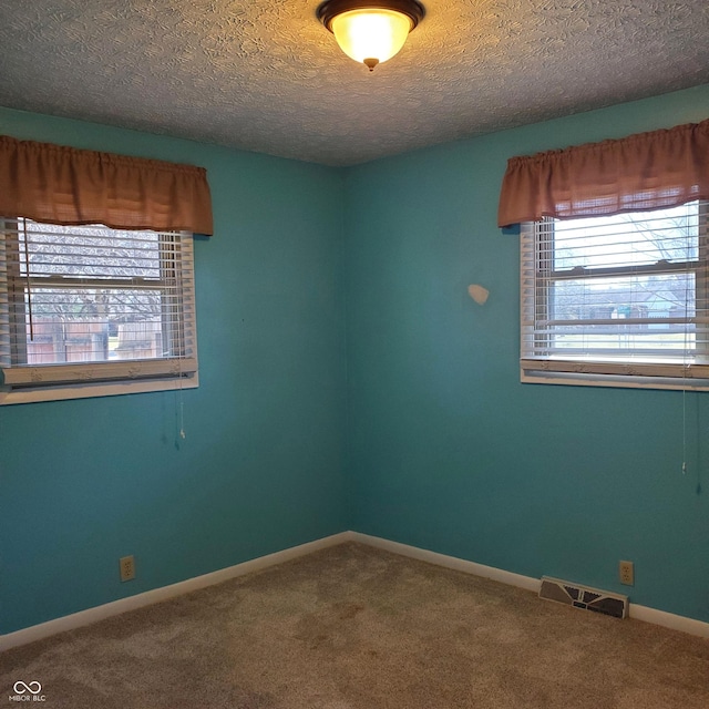 carpeted empty room featuring visible vents, a textured ceiling, and baseboards