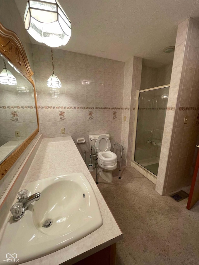 bathroom featuring a shower with shower door, tile walls, vanity, toilet, and a textured ceiling