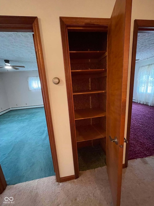 hallway with baseboard heating, light carpet, and a textured ceiling