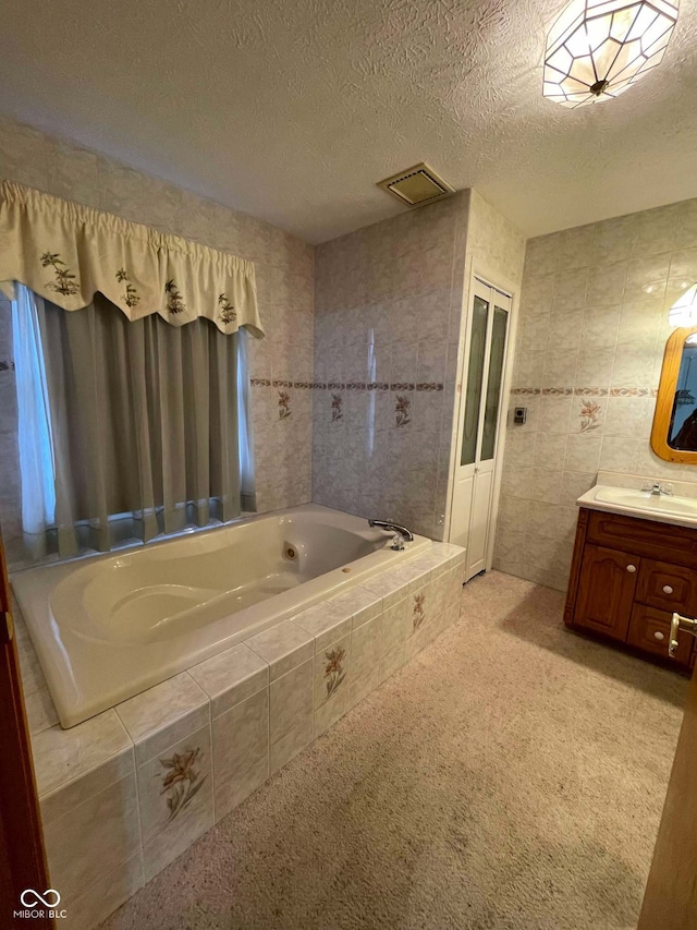 bathroom with vanity, tile walls, a textured ceiling, and tiled bath