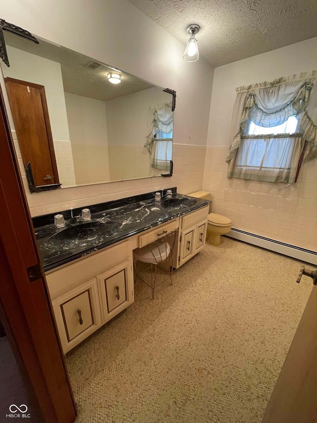 bathroom with tile walls, vanity, a baseboard heating unit, toilet, and a textured ceiling