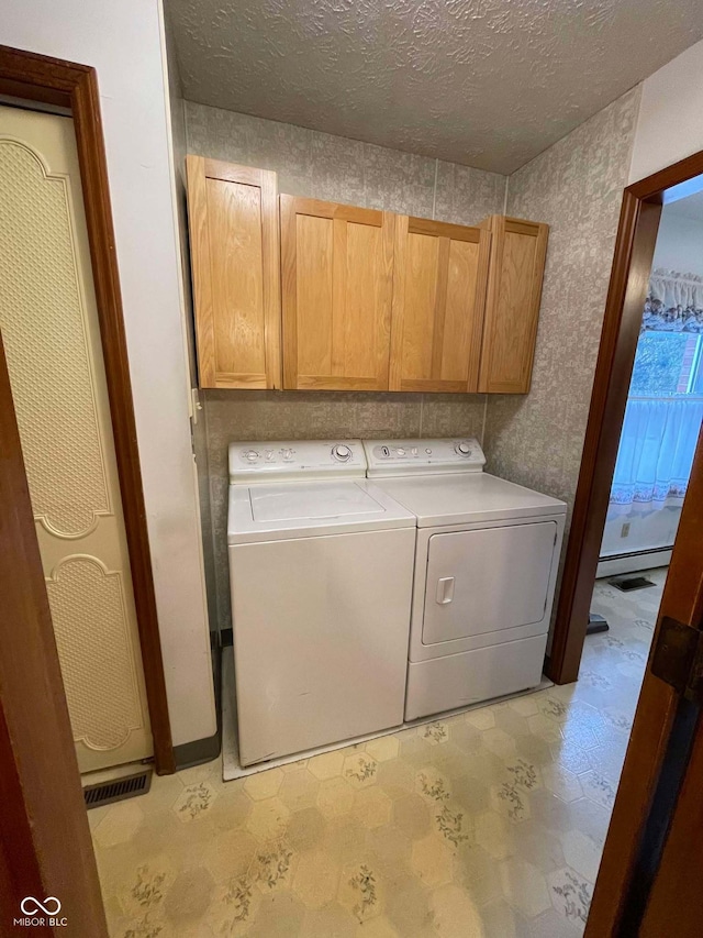 washroom featuring cabinets, washing machine and clothes dryer, a textured ceiling, and a baseboard heating unit