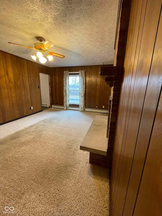 unfurnished living room featuring wood walls, light carpet, a textured ceiling, a baseboard radiator, and ceiling fan