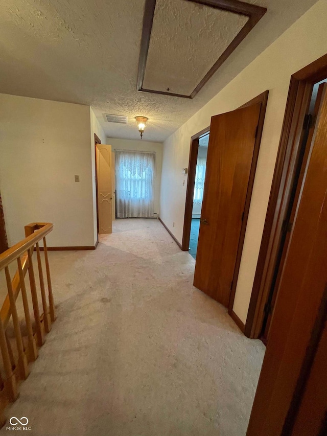 hallway with light carpet and a textured ceiling