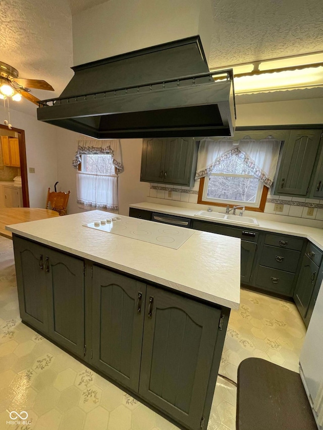 kitchen featuring sink, ceiling fan, a textured ceiling, a kitchen island, and washing machine and clothes dryer