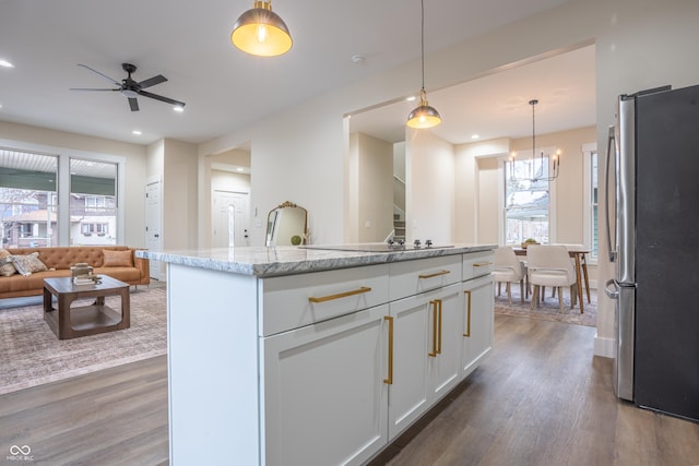 kitchen with stainless steel refrigerator, white cabinetry, hanging light fixtures, light stone countertops, and dark wood-type flooring