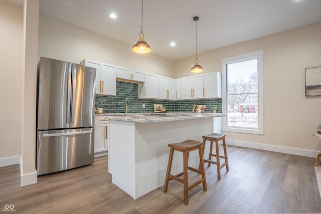 kitchen with stainless steel refrigerator, white cabinetry, hanging light fixtures, a center island, and light stone countertops