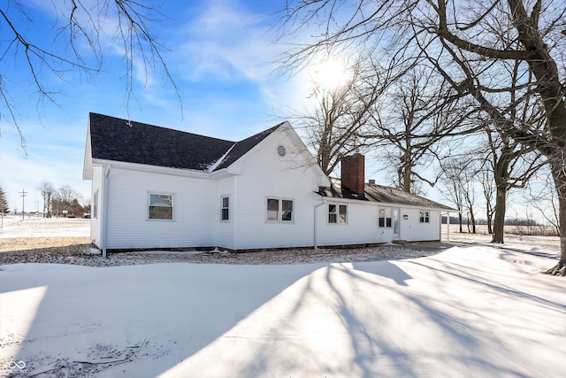 snow covered house with roof with shingles and a chimney