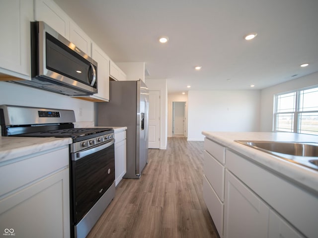 kitchen featuring appliances with stainless steel finishes, light wood-style floors, white cabinetry, a sink, and recessed lighting