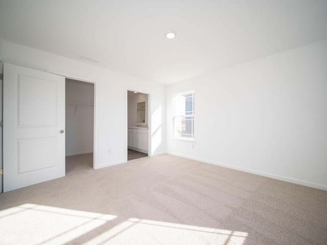 unfurnished bedroom featuring baseboards, ensuite bathroom, a walk in closet, carpet flooring, and a closet