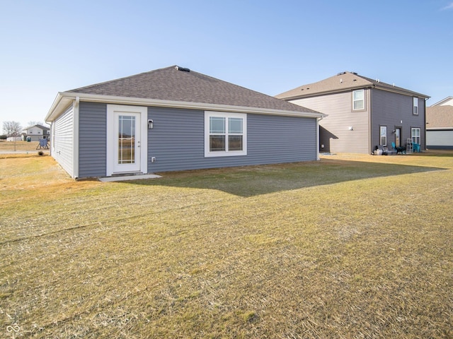 rear view of property with a shingled roof and a lawn