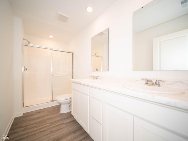 bathroom with visible vents, toilet, a stall shower, a sink, and wood finished floors