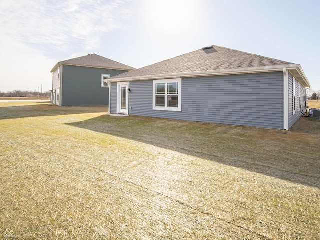 rear view of property featuring a shingled roof and a lawn