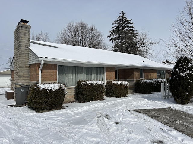 view of snowy exterior with a garage, brick siding, a chimney, and fence