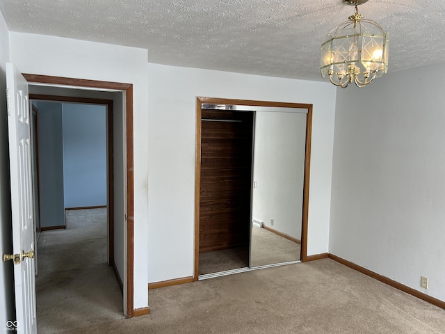 unfurnished bedroom with an inviting chandelier, a closet, carpet, a textured ceiling, and baseboards