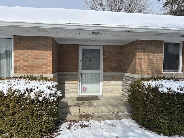 snow covered property entrance featuring brick siding