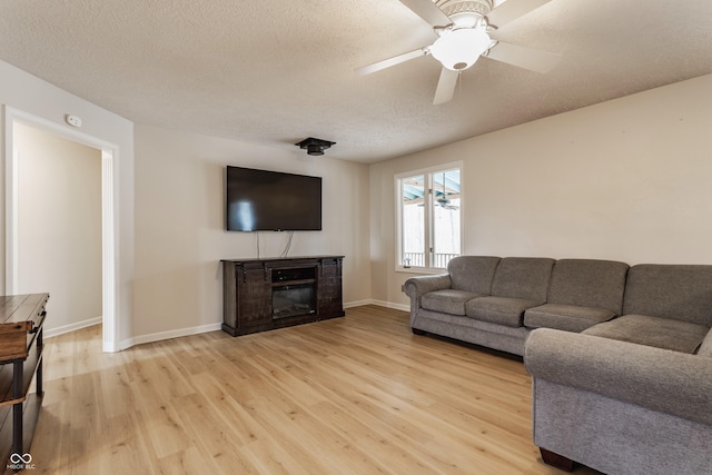 living area with baseboards, ceiling fan, light wood-style floors, a glass covered fireplace, and a textured ceiling